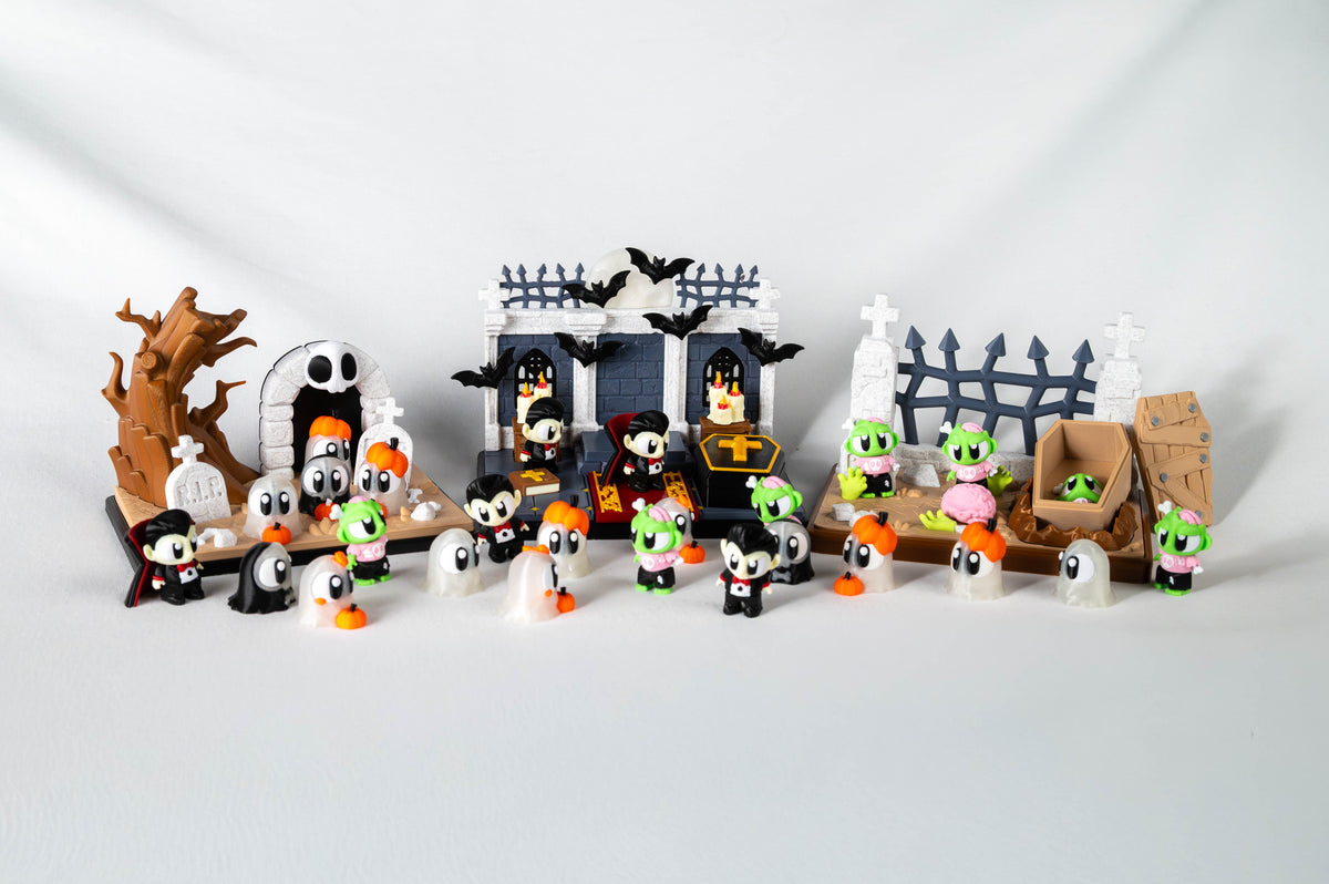 A Halloween-themed toy set featuring small character figures, tombstones, a spooky house, a bare tree, and a fence, arranged on a light gray studio background.