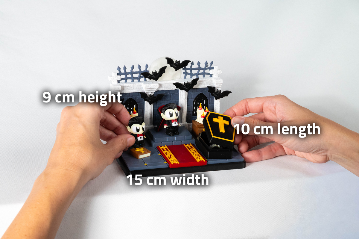 A hands-on view of a small Halloween-themed building block display with two figures, bats, a tombstone, and a fence, overlaid with size labels reading 9 cm height, 10 cm length, and 15 cm width on a white background.